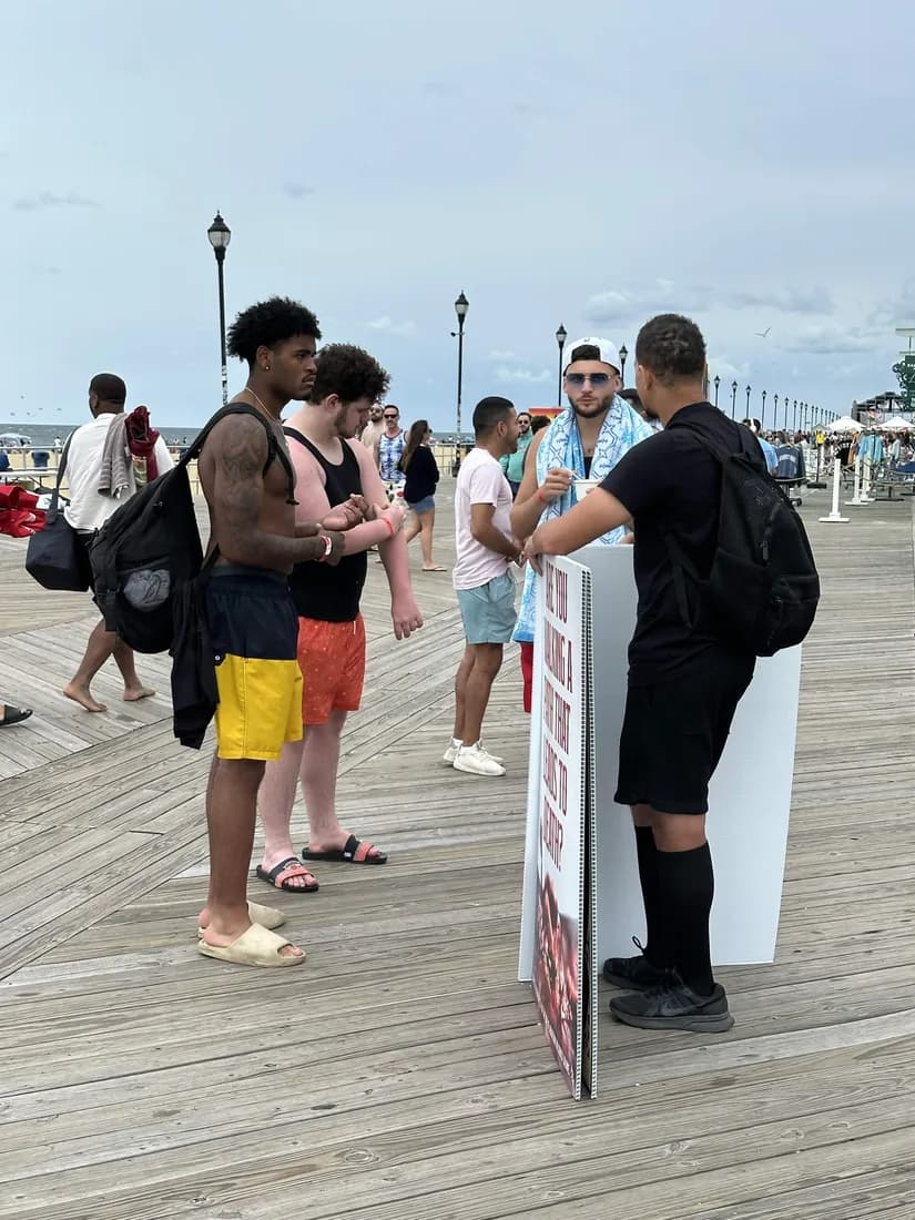 An abolitionist holding a sign and talking with a group of young men on a seaside boardwalk.